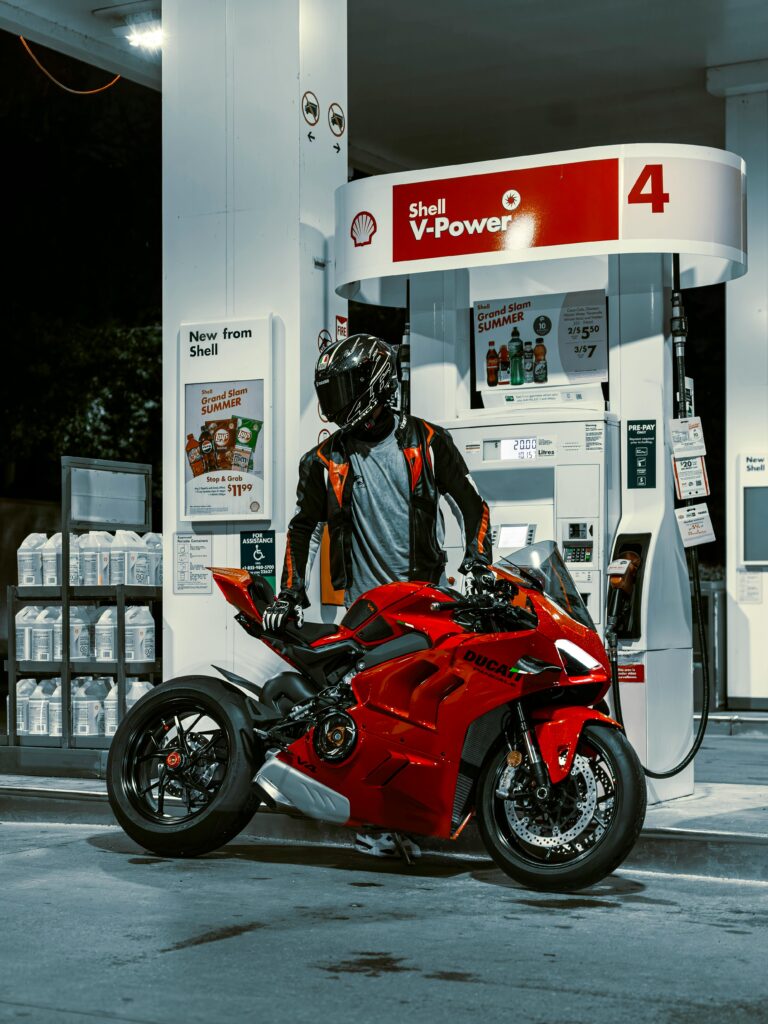 Services Rider beside red Ducati motorbike refueling at Shell station at night.